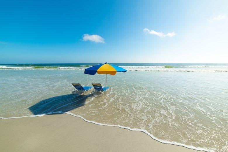 two loungers in the water on the sand with a beach umbrella waiting for you to relax in.