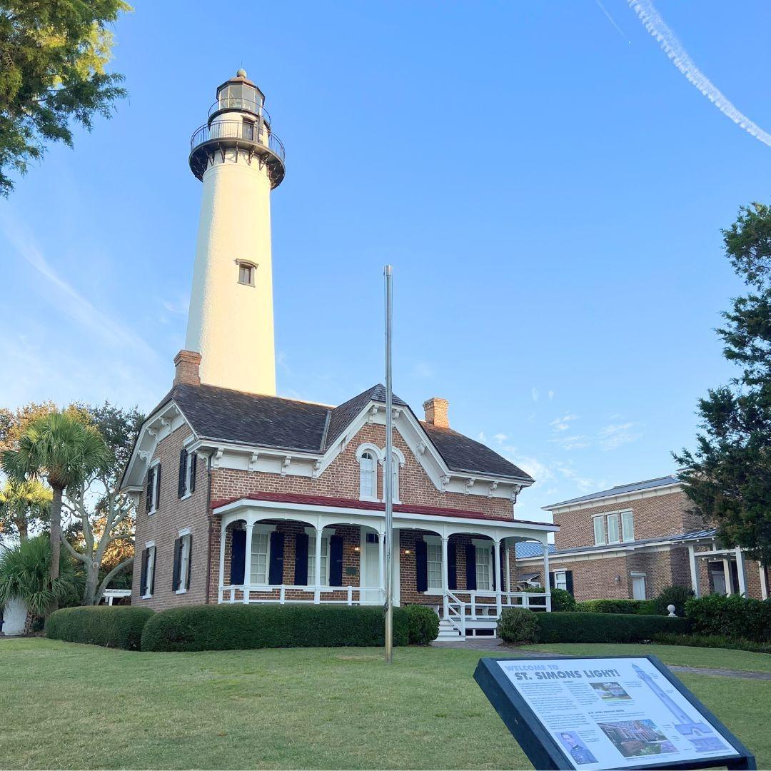 St. Simons Lighthouse and Keeper's House on St. Simons Island under a clear blue sky.