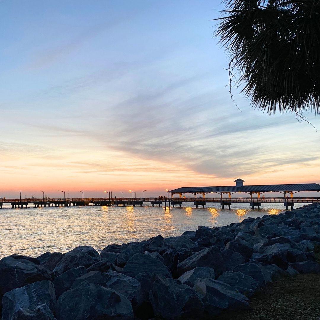 St. Simons Island Pier at sunset with calm water, rocky shoreline, and colorful evening sky.
